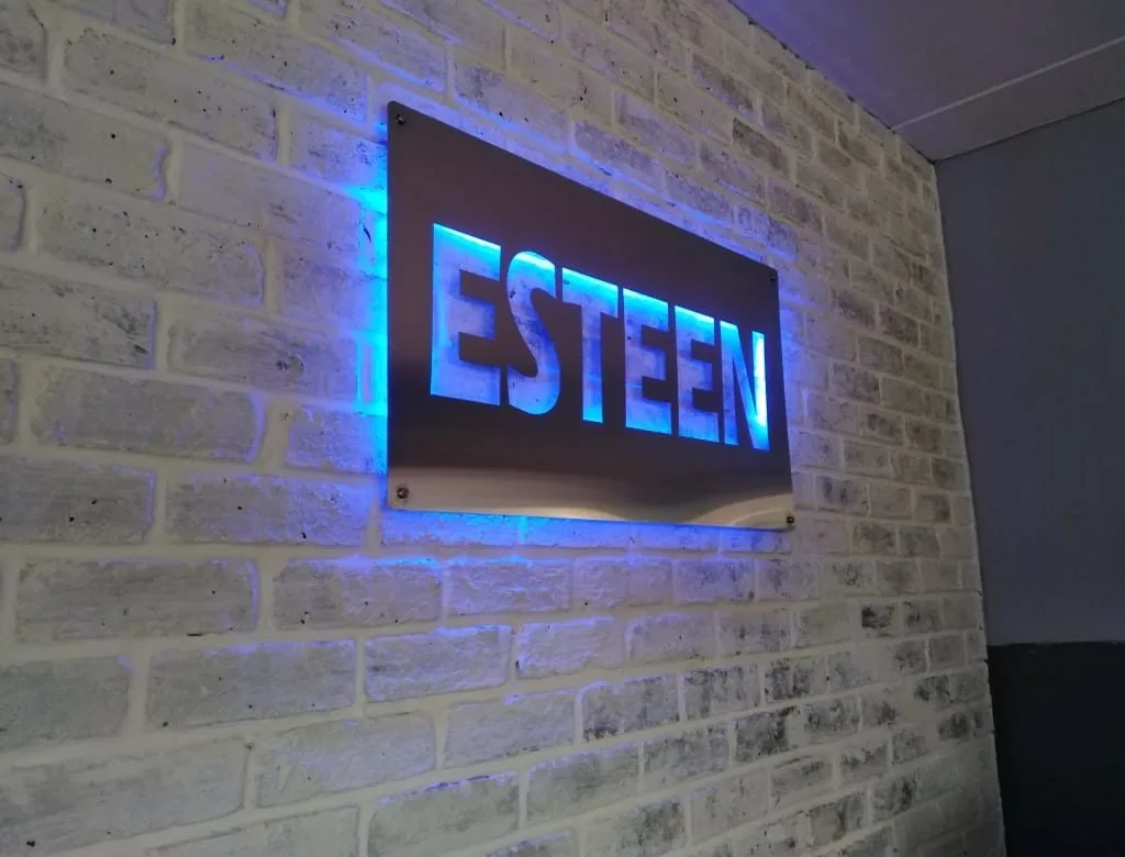 Blue backlit Esteem sign mounted on a brick wall