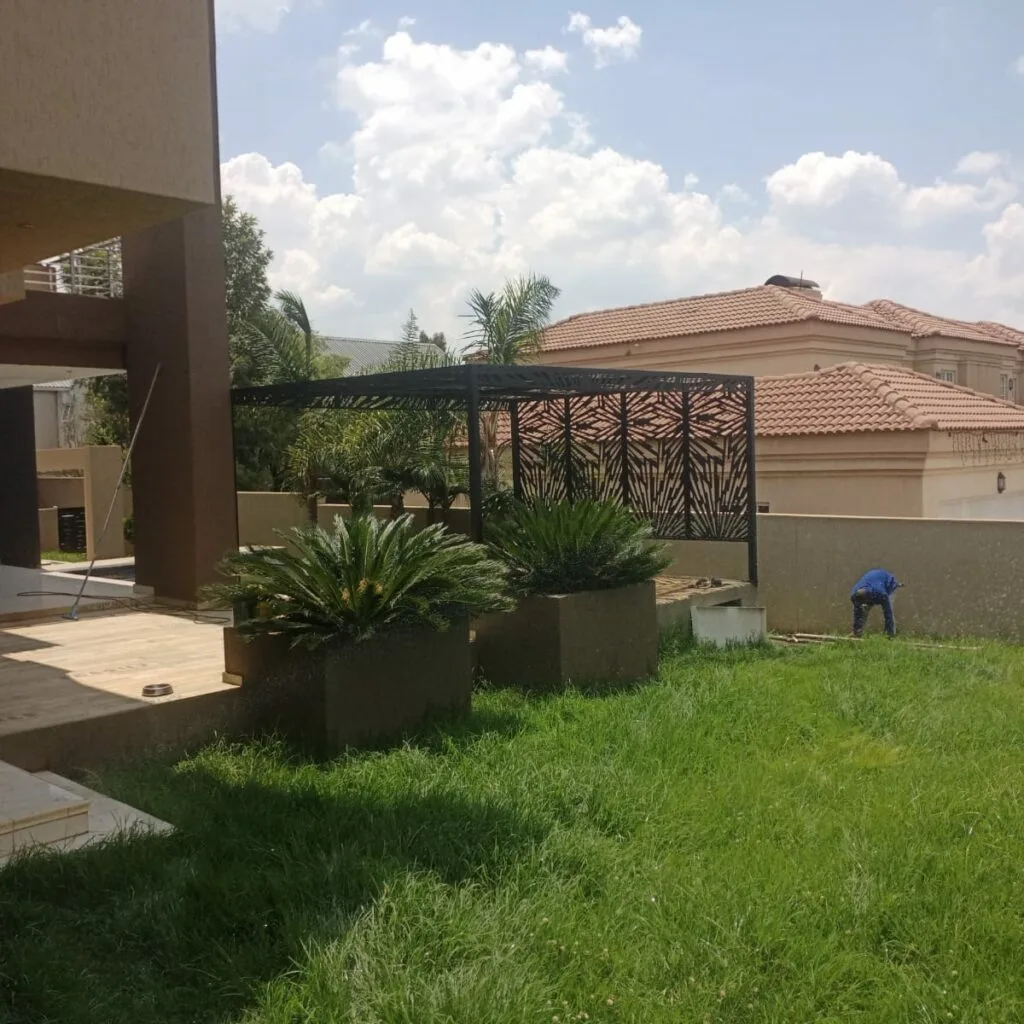 Steel pergola with patterned panels beside a landscaped garden