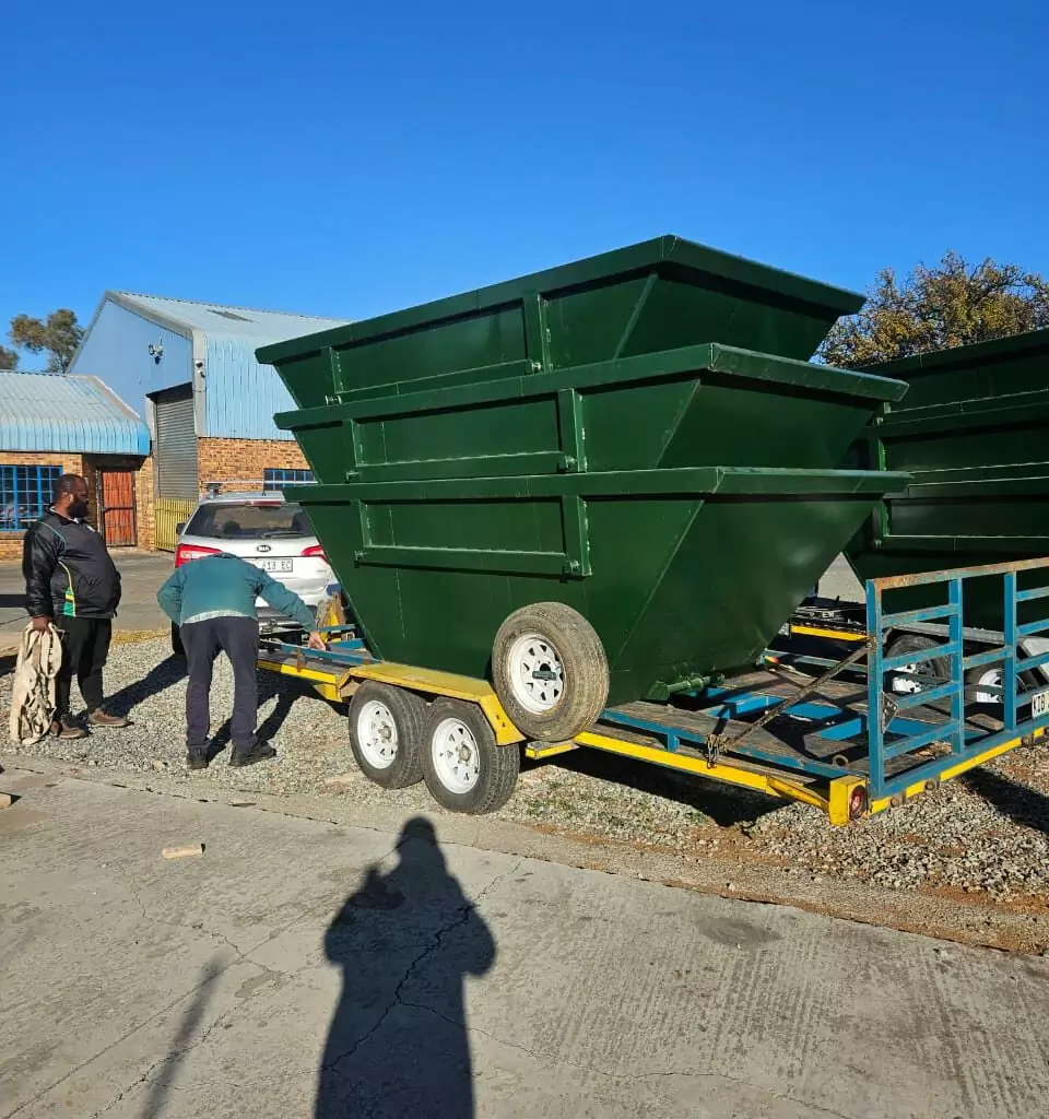 Green steel skip bins on a trailer outside a workshop