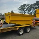 Yellow steel skip bins carried on a tandem-axle trailer